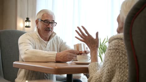 Senior-Man-Giving-a-Gift-to-Woman-at-Cafe-Date