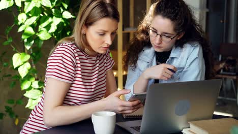 Close-up-of-two-female-students-using-smart-phone.-Attractive-blond-girl-is-touching-screen-and-chatting-with-her-friend.-Modern-technology-for-young-people-concept.