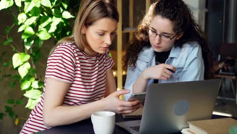 Nahaufnahme-von-zwei-Studentinnen-mit-Smartphone.-Attraktive-Blondine-ist-Bildschirm-berühren-und-im-Chat-mit-ihrer-Freundin.-Moderne-Technik-für-Jugendliche-Konzept.