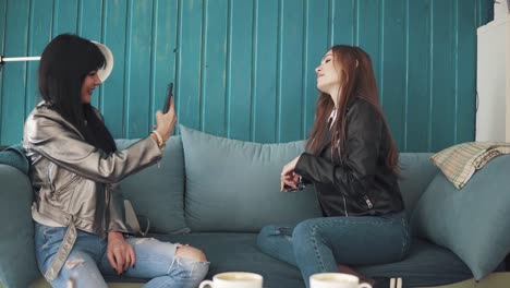 two-funny-girls-are-photographing-each-other-on-the-camera-of-a-smartphone-in-a-cafe.-fashion-girls-spend-time-together