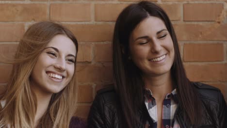 two-beautiful-women-in-front-of-brick-wall-smiling.-shot-in-slow-motion