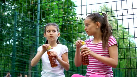 Zwei-kaukasischen-Kinder-sagen,-Geheimnisse,-lachen-und-trinken-im-Park,-im-Freien.