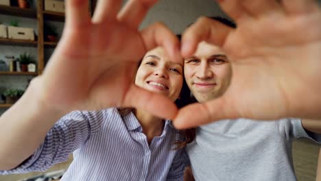 Portrait-of-cheerful-multiethnic-couple-making-heart-with-their-hands,-looking-at-camera-and-smiling.-Romantic-relationship,-married-life-and-honeymoon-concept.