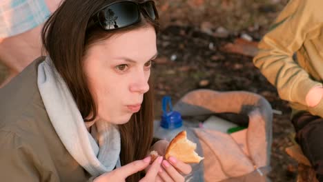 Jovencita-morena-comiendo-pan-y-carne-frita-en-el-fuego.-Viaje-de-camping.