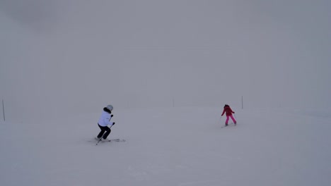 Two-Female-Skiers-Skiing-On-The-Mountain-Downhill-In-Winter-In-Heavy-Fog