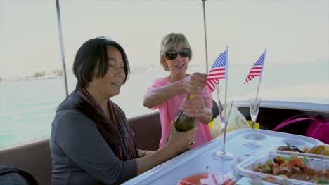 multiracial-older-women-opening-champagne-and-celebrating-on-a-boat