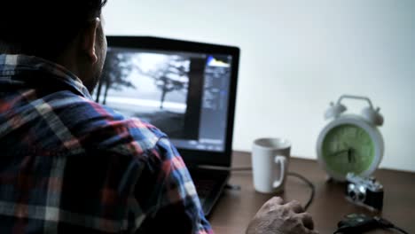 Back-view-of-male-photographer-working-at-home-on-laptop,-retouching-photos