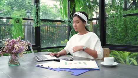 Hermosa-joven-sonriente-mujer-asiática-trabajando-en-ordenador-portátil-mientras-disfruta-de-beber-café-en-sala-de-estar-en-casa.-Mujer-de-negocios-asiática-trabajo-Finanzas-de-documento-en-la-oficina-en-casa.-Disfrutando-en-casa.