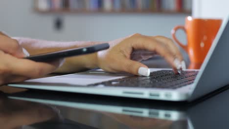 Primer-plano-de-mujer-mano-escribiendo-en-el-portátil-y-el-uso-de-smartphone