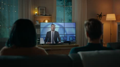 Paar-Uhren-Abendnachrichten-im-Fernsehen-beim-Sitzen-auf-einer-Couch-zu-Hause-am-Abend.-Verliebte-Menschen-verbringen-Zeit-miteinander.-Rückansicht-Schuss.