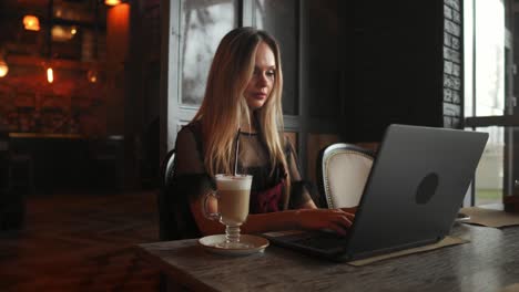 Vista-lateral.-Mujer-de-negocios-joven-sentado-en-la-mesa-y-tomar-notas-en-el-cuaderno.-En-la-tabla-es-portátil,-smartphone-y-taza-de-café.-Gráficos-de-pantalla-de-ordenador-y-cartas.-Aprendizaje-en-línea-de-los-estudiantes.-Blogger