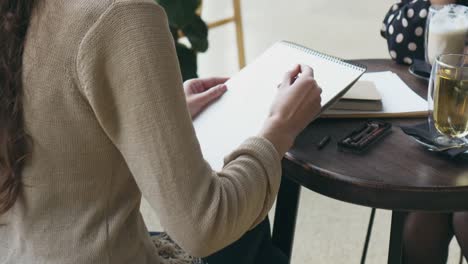 Woman-drawing-sketch-and-talking-with-friend-at-cafe