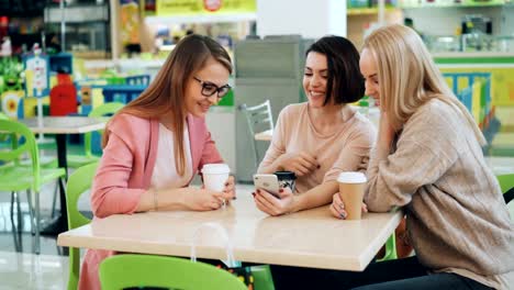 Modern-girls-are-using-smartphone-together-sitting-in-cafe-and-looking-at-screen-then-doing-high-five-and-laughing.-Modern-technology-and-friendship-concept.