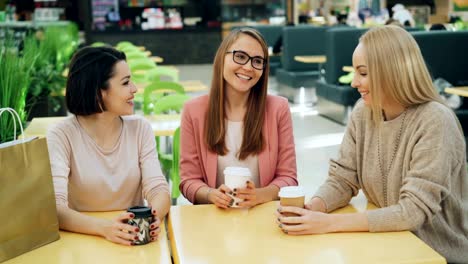 Gruppe-der-glückliche-junge-Damen-ist-plaudern-und-Lachen-mit-to-Go-Getränke-am-Tisch-im-Einkaufszentrum-Café-sitzen-und-Geselligkeit.-Lifestyle-und-Spaß-Jugendkonzept.