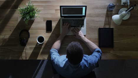 Top-View-of-Male-Programmer-Writing-Code-on-His-Desktop-Computer-at-Night.-His-Table-is-Illuminated-by-Cold-Blue-Light-From-Outside.