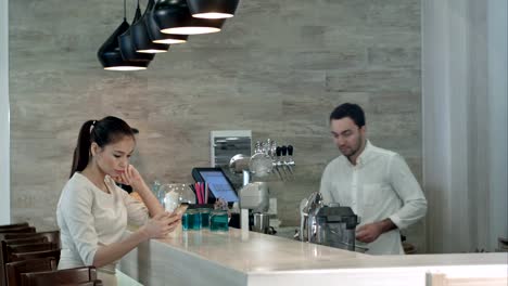 Smiling-young-woman-drinking-coffee-at-the-counter-and-talking-to-the-bartender