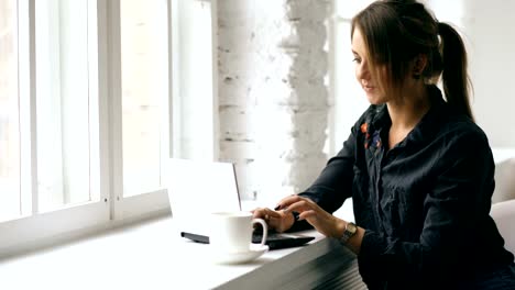 Junge-lächelnde-Studentin-sitzt-in-Café-am-Tisch-mit-Laptop-drinnen