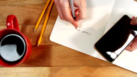 Hand-of-businesswoman-writing-on-book-at-desk