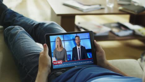 Entspannter-Mann-Lying-auf-His-Couch-Watches-News-Broadcast-auf-seinem-Tablet-Computer.