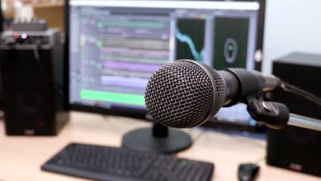 Microphone-on-the-background-of-the-computer-monitor.-Home-recording-Studio.-Close-up.-The-focus-in-the-foreground.-Blurred-background.-Software-for-recording-and-editing-sounds.-4K,-UHD,-Ultra-HD