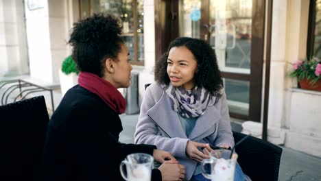 Two-attractive-mixed-race-women-talking-and-drinking-coffee-in-street-cafe.-Friends-have-fun-after-visiting-mall-sale
