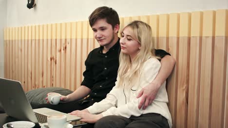 Beautiful-young-couple-with-laptop-in-cafe,-they-are-watching-movie-and-drinking-coffee-together