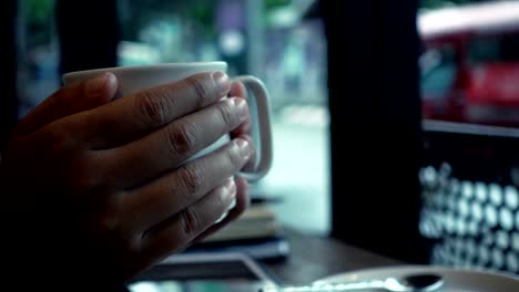 Woman-hand-holding-a-cup-of-coffee-in-the-cafe-in-the-rainy-day