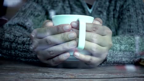 Mano-de-mujer-sosteniendo-una-taza-de-café-en-la-cafetería-en-el-día-de-lluvia