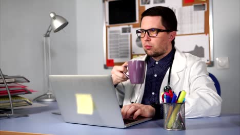 Male-doctor-working-on-his-workplacean-and-have-a-break-to-drink-some-coffee.