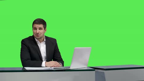 Media-broadcaster-is-sitting-at-a-table-and-talking-on-a-mock-up-green-screen-in-the-background.