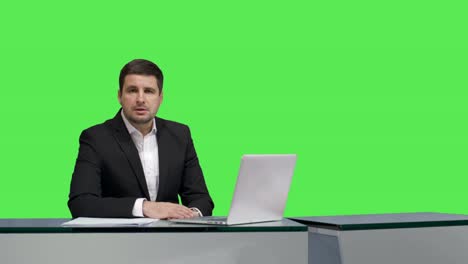 Media-broadcaster-is-sitting-at-a-table-and-talking-on-a-mock-up-green-screen-in-the-background.