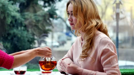 Blonde-enjoying-hot-tea-and-talks-with-friend-in-cafe