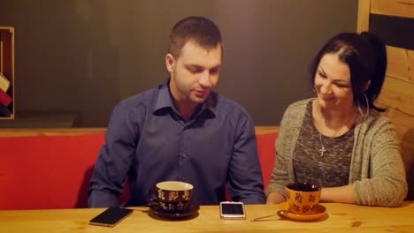 Una-pareja-sentada-en-un-café,-hablar,-bebe-café-y-mirando-el-teléfono