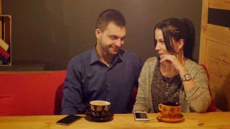 Una-pareja-sentada-en-un-café,-hablar,-bebe-café-y-mirando-el-teléfono