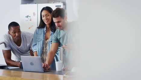 Friends-Looking-At-Laptop-And-Drinking-Coffee-In-Modern-Kitchen