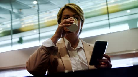 Businesswoman-holding-mobile-phone-and-drinking-coffee