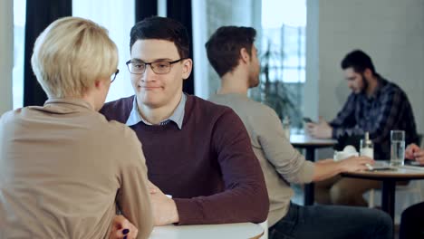 Young-couple-talking-and-drinking-coffee-near-the-window-in-cafe