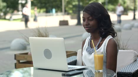 Young-african-woman-sitting-alone-in-a-cafe-having-a-videoconferance-on-a-laptop