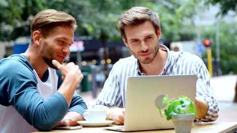 Freunde-diskutieren-über-Laptop-beim-Kaffeetrinken-im-Café-4k