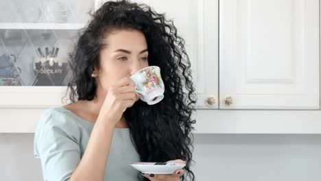 Smiling-woman-drinks-coffee-in-the-kitchen