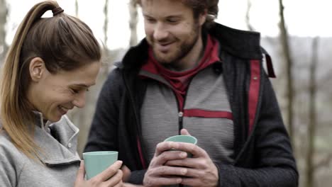 Woman-bringing-hot-beverage-or-coffee-or-tea-to-man-in-camping-place.-Couple-people-in-love-autumn-outdoor-trip-in-nature.-Fall-sunny-day.-4k-slow-motion-video