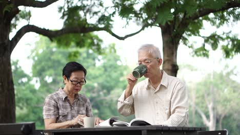 Asian-senior-retire-couple-drink-coffee-and-read-book-in-park