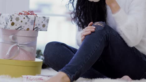 Young-girl-with-cup-sits-on-floor-near-christmas-gifts