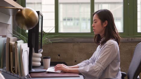 Mujer-asiática-joven-usando-la-computadora-en-una-oficina,-vista-lateral