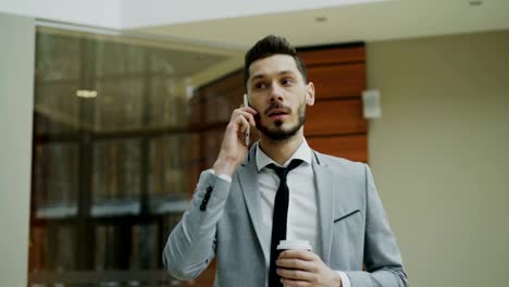 Stedicam-shot-of-businessman-talking-with-smartphone-and-walking-in-modern-office-hall