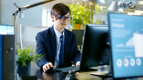 In-the-Office-Agitated-Businessman-works-on-a-Desktop-Personal-Computer,-He's-Overworked-and-Drinks-Coffee.-His-Colleague's-Computer-Shows-Infographics