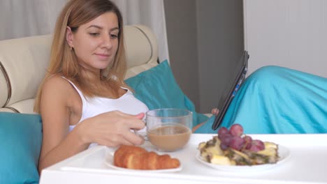 Mujer-joven-con-el-portátil-en-casa-desayunando-en-la-cama-y-tomar-café.