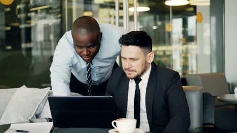 Zwei-Geschäftspartner-diskutieren-aktiv-ihre-Startprojekt-in-stilvollen-Café-sitzen.-Bärtige-Geschäftsmann-sitzt-Ang-sprechen-seine-Kollegin-beim-betrachten-Laptop-computer