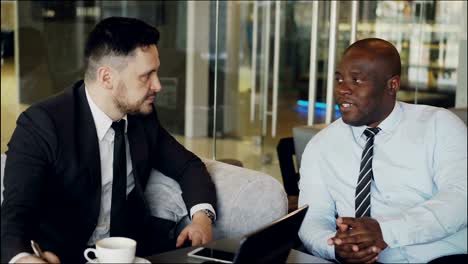 Two-confident-business-colleagues-discussing-about-partnership-during-meeting-in-modern-cafe