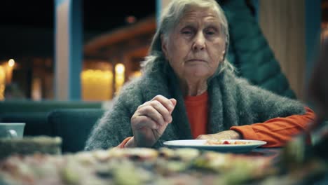 Beautiful-elderly-woman-is-sitting-in-restaurant-and-eats-pizza.-Female-cuts-the-pizza-into-pieces-in-cafe